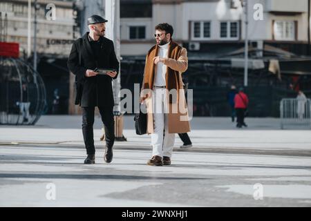 Deux hommes à la mode participent à une réunion d'affaires en plein air décontractée dans un cadre urbain, à l'aide d'une tablette numérique pour la collaboration. Banque D'Images