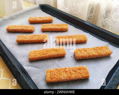 Les bâtonnets de poisson congelés sont disposés sur du papier sulfurisé. Cuisson d'une délicatesse de poisson. Papier cuisson sur une plaque à pâtisserie. Un déjeuner rapide du four. Menu poisson Banque D'Images