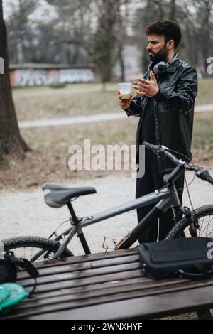 Homme d'affaires contemplatif avec café prenant une pause dans le parc avec son vélo Banque D'Images