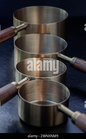 Ensemble de tasses à mesurer en laiton avec poignées en bois avec conception de trou suspendu sur fond sombre. Tasses et cuillères à mesurer en bois et en laiton pour mesurer un sec an Banque D'Images