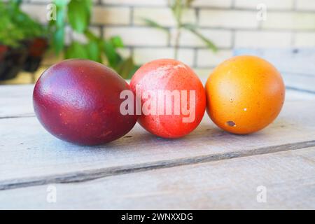 Gros plan sur les oeufs colorés de Pâques sur la table en bois, fond pascal. Trois œufs de poule durs avec coquilles rouges, oranges et brunes, teints avec de l'écorce d'oignon. Banque D'Images