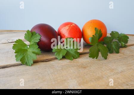 Gros plan d'oeufs colorés de Pâques sur fond en bois. Trois œufs de poule durs avec coquilles rouges, oranges et brunes, teints avec de l'écorce d'oignon. Vert frais Banque D'Images
