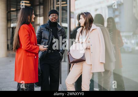 Trois jeunes gens d'affaires divers se tiennent à l'extérieur, engagés dans la conversation avec des sourires lumineux, vêtus d'une tenue d'affaires décontractée et élégante. Banque D'Images