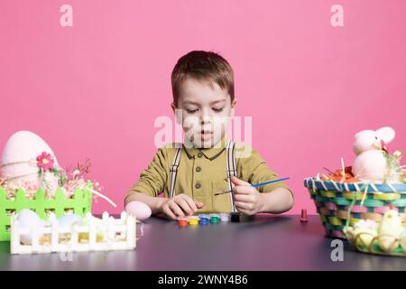 Joyeux petit enfant décorant des œufs et des ornements avec de l'aquarelle, de la coloration et des décorations artisanales à temps pour la célébration du dimanche de pâques. Jeune garçon joyeux peignant avec la teinture de cravate. Banque D'Images