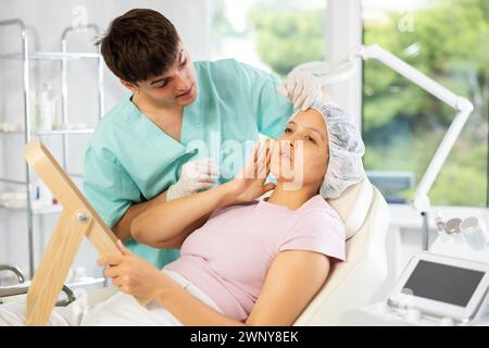 Jeune cosmétologue masculin examine le visage de la jeune femme Banque D'Images