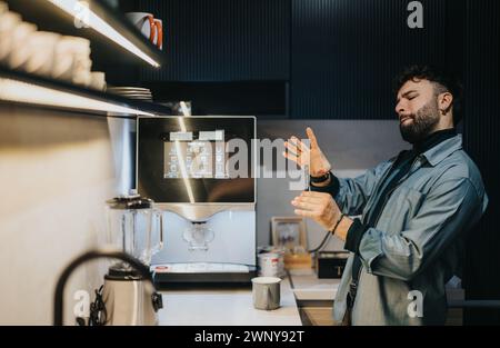 Jeune homme impatient vérifiant montre-bracelet en attendant le café dans la cuisine moderne avec machine à expresso. Banque D'Images