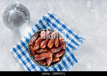 Dattes séchées dans un bol et un verre d'eau sur une serviette en lin, nourriture Ramadan, espace copie, vue de dessus Banque D'Images