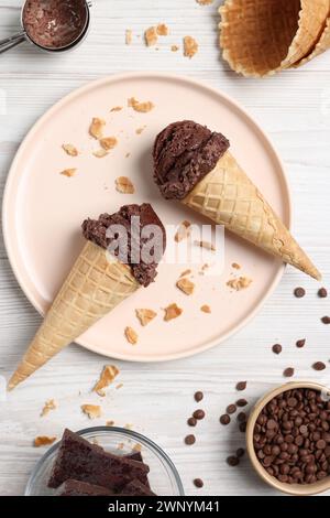 Cuillères à crème glacée au chocolat dans des cônes de gaufrettes et des bonbons sur une table en bois clair, pose à plat Banque D'Images
