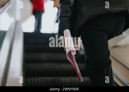 Plan précis du côté d'un individu avec une montre, grimpant dans un escalier roulant, saisissant un document enroulé ou un plan. Banque D'Images