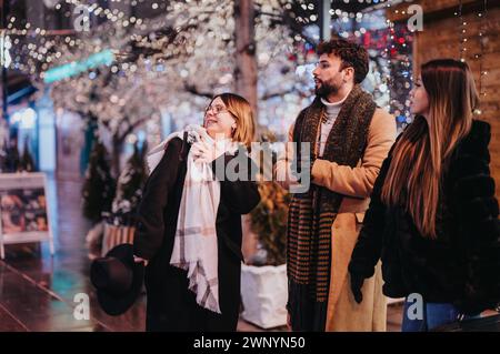 Groupe d'amis engagés partageant une conversation et riant dans une rue décorée de façon festive, évoquant la chaleur et la convivialité. Banque D'Images