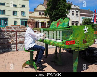 Sremska Mitrovica, Serbie, 05 juin 2021. Un garçon dans une chemise blanche joue le piano dans la rue. L'enfant a 9 ans de race blanche. Vert peint au piano Banque D'Images