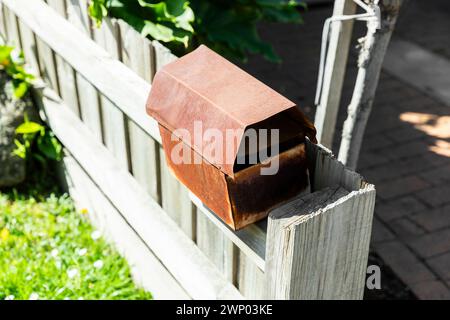 Vue rapprochée d'une vieille boîte aux lettres rouillée montée sur une clôture en bois. Banque D'Images