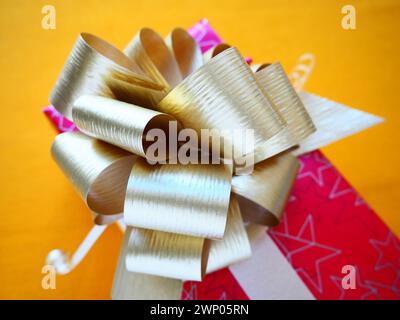 Boîte cadeau rose rouge avec un grand noeud doré sur un fond jaune ocre. Cadeau de Noël, nouvel an, anniversaire, Fête des mères, mariage, Saint-Valentin Banque D'Images