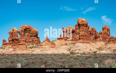 Des nodules et des tours de grès coiffés de chapeaux s'élèvent d'une base de sable pâle au-dessus d'une plaine de broussailles d'artemisia sous un ciel bleu et un ciel nuageux fin dans le parc national des Arches, Utah. Banque D'Images