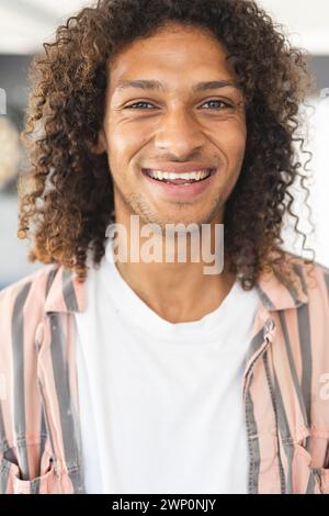 Un jeune homme biracial aux cheveux bruns bouclés sourit chaleureusement Banque D'Images