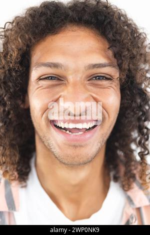 Jeune homme biracial aux cheveux bouclés sourit largement, mettant en valeur la joie Banque D'Images