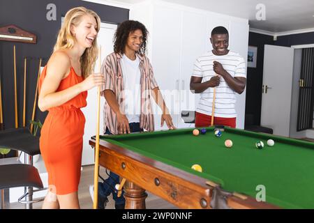 Jeune femme caucasienne dans une robe rouge joue au billard avec un homme biracial et un homme afro-américain Banque D'Images