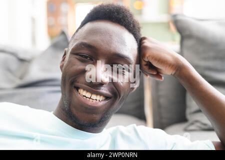 Jeune homme afro-américain avec un sourire éclatant, se reposant dans un cadre intérieur décontracté Banque D'Images