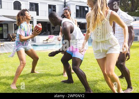 Groupe diversifié d'amis profiter d'un jeu de football ludique dans une cour arrière ensoleillée Banque D'Images