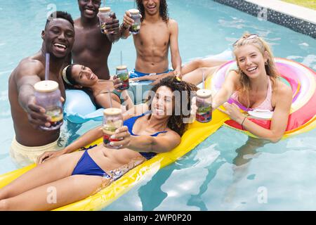 Groupe diversifié d'amis profitant d'une fête à la piscine, griller des boissons Banque D'Images
