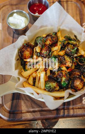 Une assiette de nourriture avec des frites et des choux de bruxelles. L'assiette est sur une table en bois Banque D'Images