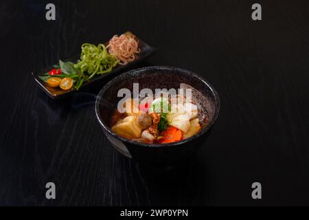 Bun Rieu Chay, soupe de vermicelles en pâte végétalienne avec crevettes hachées, tofu, tomate, pâte de crevettes, nourriture vietnamienne isolée sur fond de table en bois noir Banque D'Images