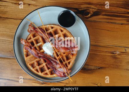 Une assiette de bacon et de gaufres avec un côté de sirop. L'assiette est sur une table en bois Banque D'Images