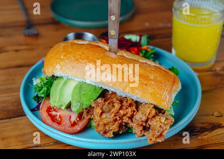 Un sandwich avec avocat et tomate sur une assiette bleue. Un couteau sort du sandwich Banque D'Images