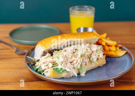 Un sandwich avec laitue et tomate sur une assiette bleue. Un verre de jus d'orange est sur la table Banque D'Images