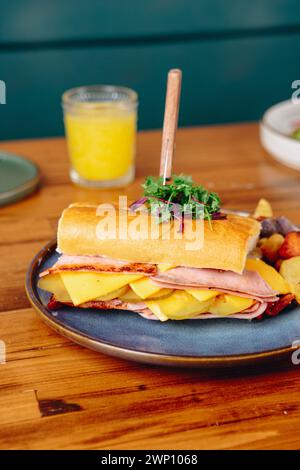 Un sandwich avec jambon et fromage sur une assiette bleue avec un verre de jus d'orange. Le sandwich est garni de persil et d'un cure-dent Banque D'Images