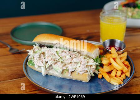 Un sandwich et des frites sont sur une assiette bleue. Le sandwich est coupé en deux et a un côté de frites. Un verre de jus d'orange est également sur la table Banque D'Images