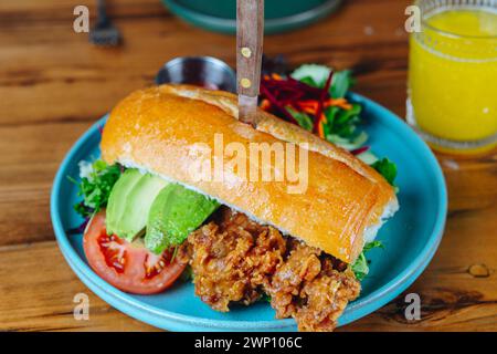 Un sandwich avec avocat et tomate sur une assiette bleue. Un couteau sort du sandwich Banque D'Images