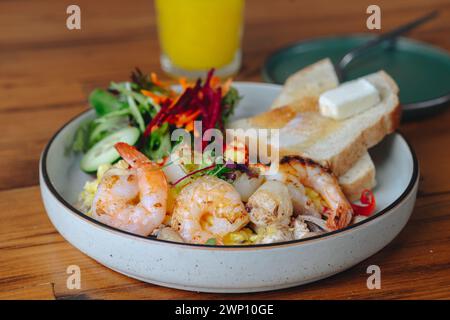 Une assiette de nourriture avec des crevettes et des légumes, et un verre de jus d'orange. L'assiette est sur une table en bois Banque D'Images