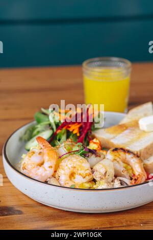 Une assiette de nourriture avec des crevettes et des légumes se trouve sur une table en bois. Un verre de jus d'orange est également présent sur la table. Concept de santé et de bien-être Banque D'Images