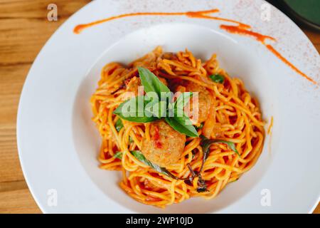 Une assiette de spaghettis avec boulettes de viande et feuilles de basilic. Le plat est servi sur une table en bois Banque D'Images