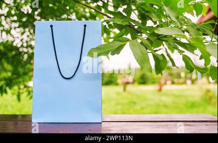 Le sac en papier vierge se trouve sur une table en bois, sur fond de feuilles vertes. Banque D'Images