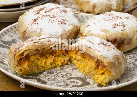 Assiette traditionnelle avec mini bastella marocaine fraîchement cuite entière et coupée en deux farcie de poulet et recouverte de sucre et de cannelle gros plan Banque D'Images