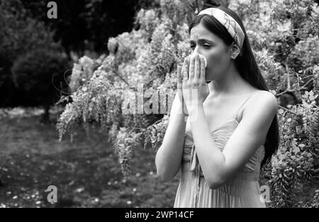 Fille souffrant d'allergie au nez éternuant. Concept de symptôme de Polen illnes. Femme allergique à la fleur au printemps floraison arbre à l'extérieur. Banque D'Images