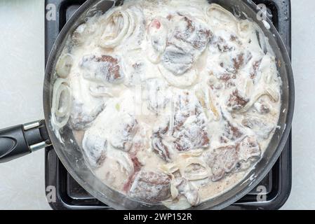 Morceaux de foie de bœuf cuits dans de la crème sure avec des oignons dans une poêle. Cuisson du foie de boeuf. Banque D'Images