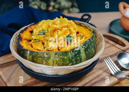 Une grande citrouille remplie d'un mélange jaune et vert de légumes. La citrouille est placée sur une table en bois avec une fourchette et une cuillère à proximité Banque D'Images