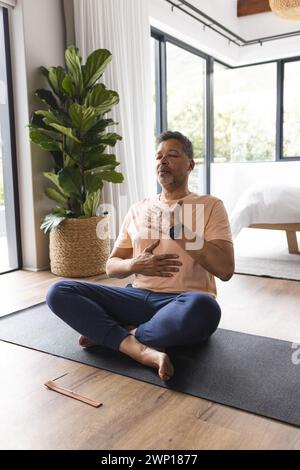 Homme senior biracial médite les yeux fermés, assis sur un tapis de yoga Banque D'Images