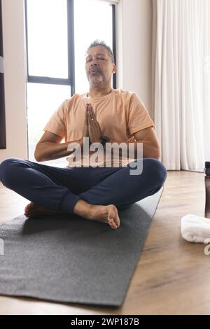 L'homme senior biracial médite avec les mains en position de prière, les yeux fermés Banque D'Images