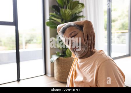 Homme senior biracial avec les cheveux gris semble avoir mal au cou, portant une chemise orange décontractée Banque D'Images