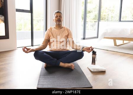 Homme senior biracial médite sur un tapis de yoga dans une pièce lumineuse Banque D'Images