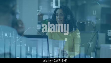 Image de graphiques financiers et de données sur femme biraciale heureuse au bureau Banque D'Images