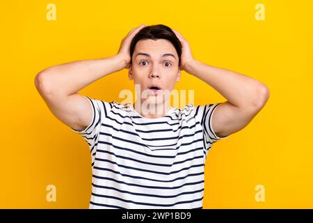 Photo d'un étudiant étonné habillé sans voix t-shirt rayé tenant les paumes sur la tête regardant isolé sur fond de couleur jaune vif Banque D'Images