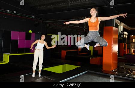 Femme d'âge moyen positive dans des vêtements sportifs sautant verticalement haut dans la salle de trampoline moderne Banque D'Images