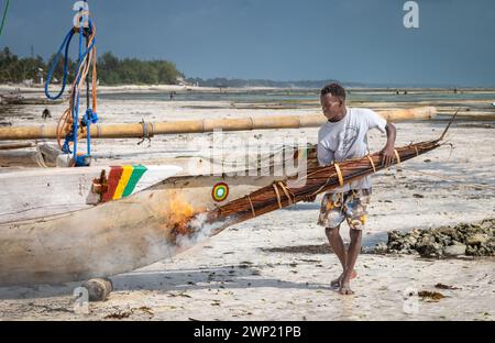 Un homme utilise des frondes de palmier brûlantes pour ébavurer et imperméabiliser son bateau traditionnel à boutre en bois, Jambiani, Zanzibar, Tanzanie Banque D'Images