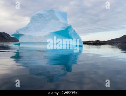 Grand iceberg de couleur bleue flotte sur l'eau calme dans la mer du fjord de Nanortalik au Groenland eau calme montrant la réflexion prise à la lumière de l'aube Banque D'Images