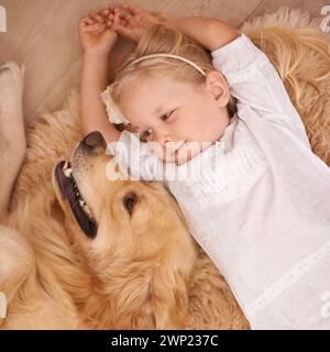 Chien, enfant et tapis sur le sol pour animal, animal de compagnie et se détendre ensemble à l'intérieur pour le lien, l'affection et l'amitié. Chiot, fille et sourire avec doré Banque D'Images